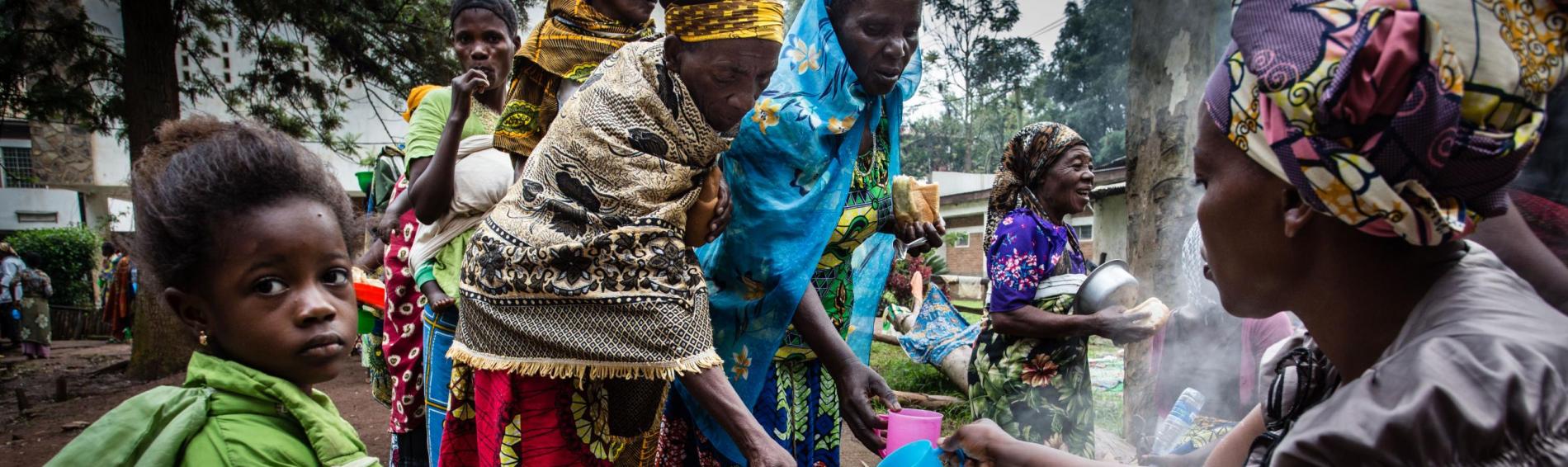 Des femmes congolaises viennent remplir leurs tasses auprès d'une autre femme, qui gère un grand bassin.