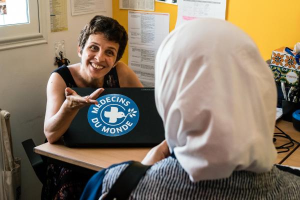 Dans les bureaux de Médecins du Monde en Tunisie, une dame voilée vue de dos regarde une autre dame souriante, installée derrière un ordinateur sur lequel apparaît le logo Médecins du Monde.