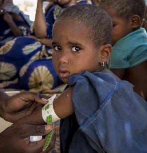Une petite fille malienne a le regard tourné vers l'objectif de la caméra alors qu'un médecin mesure la circoncéfrence de son bras.